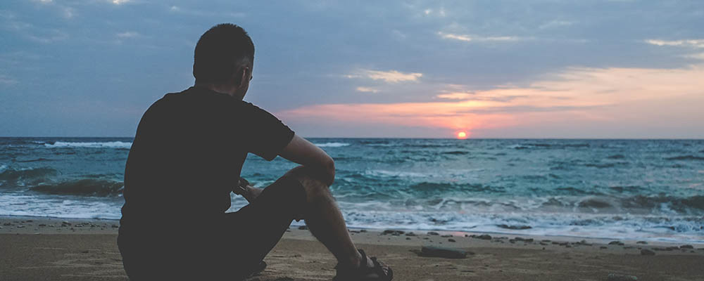 Man sitting on sand by beach at sunset
