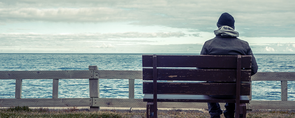 man sat on a bench looking out to sea